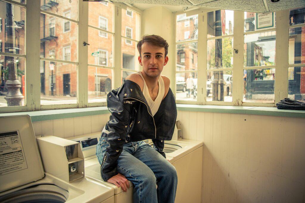 Junior Andrew Muccitelli sits atop a washing machine at Myrtle Street Laundromat. Jakob Menendez / Beacon Staff