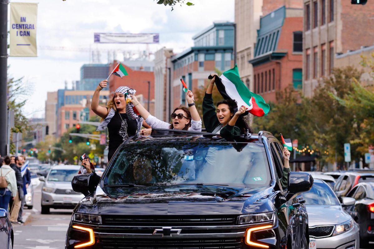 A group of pro-Palestine protestors waving Palestinian flags out of a car window. (Arthur Mansavage/Beacon Staff)