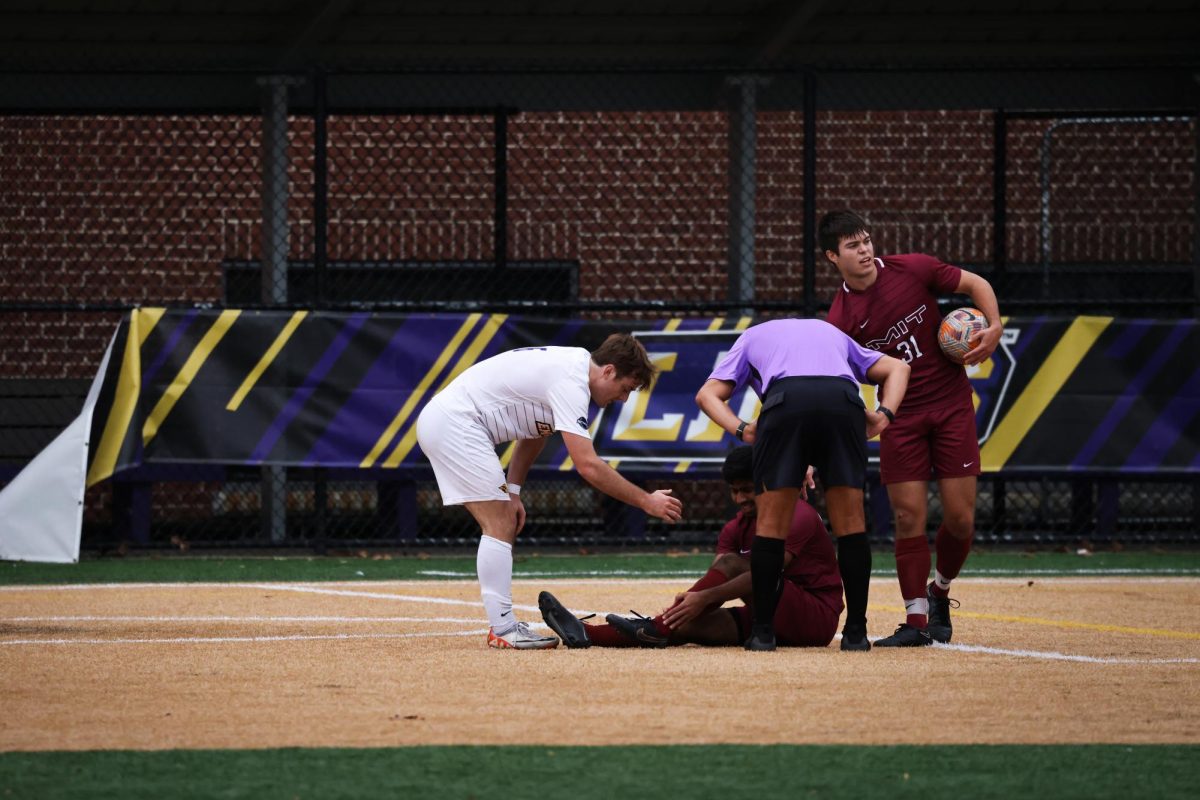 Emersons Ben Deeming (6), left, the referee, center, MITs Garrett Dyson (31), right, surround MITs Matthew Sequeira (28), who falls to the ground at Rotch Playground in Boston, on Saturday, Oct. 14, 2023. (Ashlyn Wang/Beacon Staff)