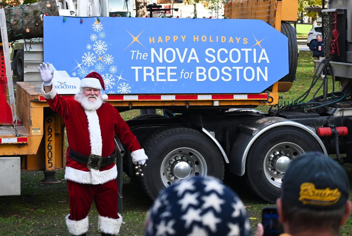 A+man+dressed+as+Santa+Claus+stands+in+front+of+the+Nova+Scotia+tree+and+greets+participants.