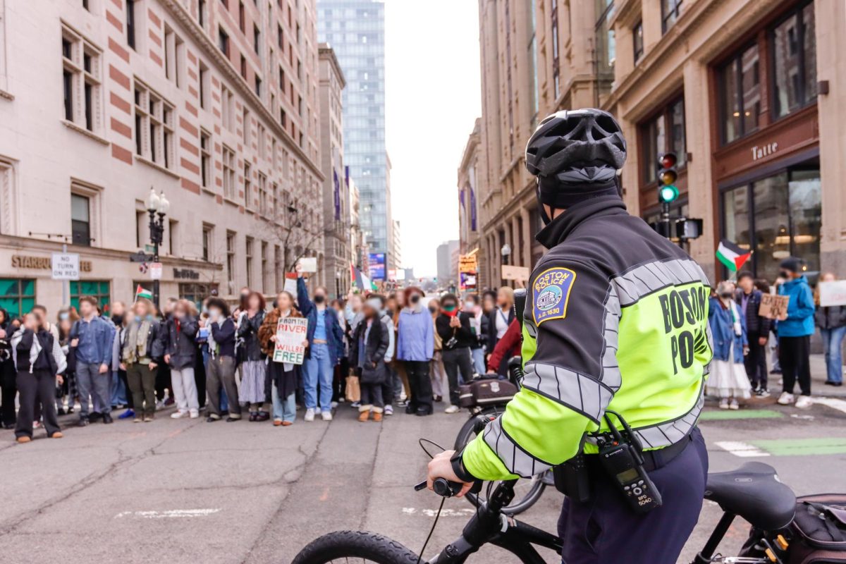 A Boston police officer stops in the intersection at Boylston and Tremont Street and observes a large crowd of protesters blocking the street. After the Emerson and Suffolk group of protesters merged, Boston police were called and watched as the group closed down the intersection. (Arthur Mansavage/Beacon Staff)