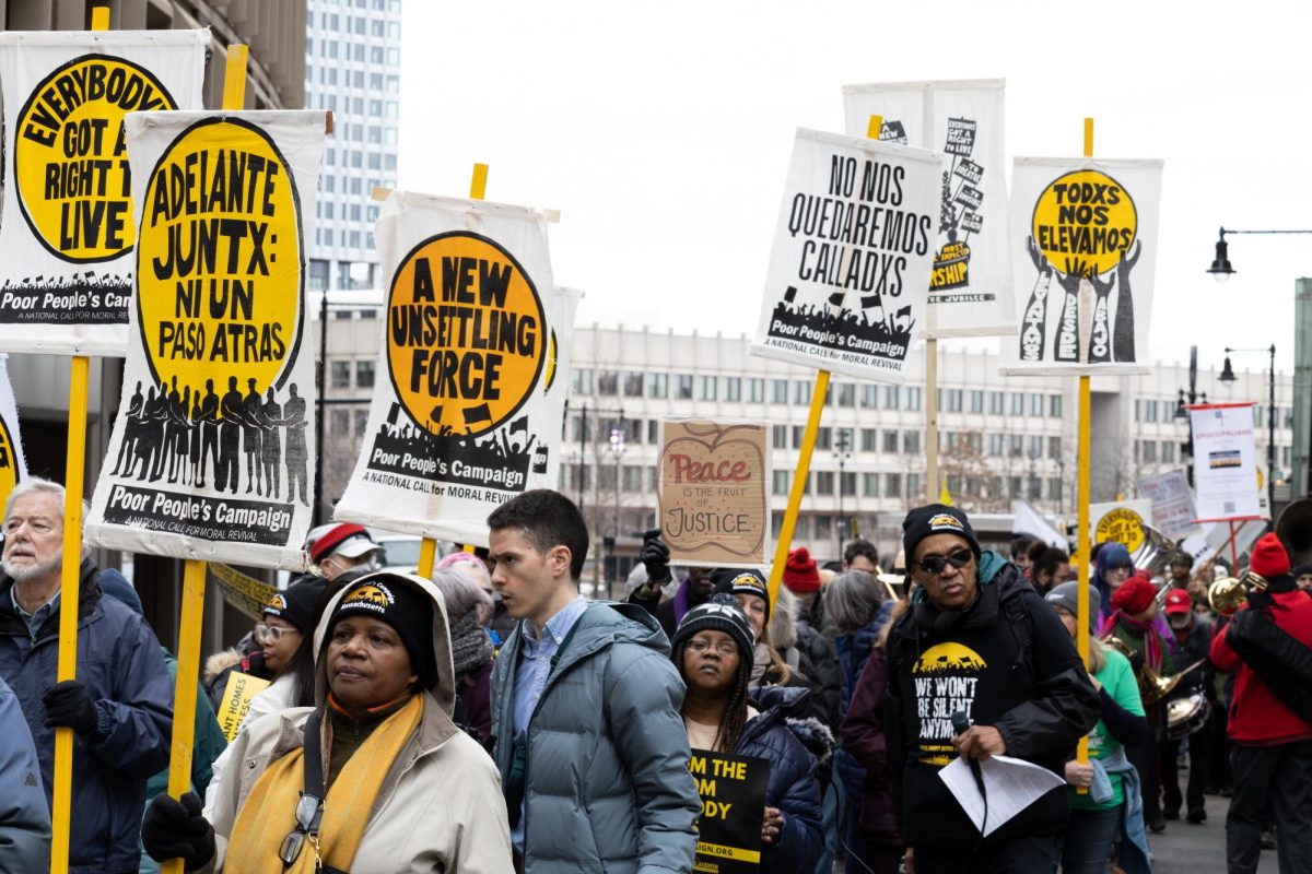 Protesters hold up signs as the march pauses in front of the Government Center. (Madla Walsh/Beacon Staff)