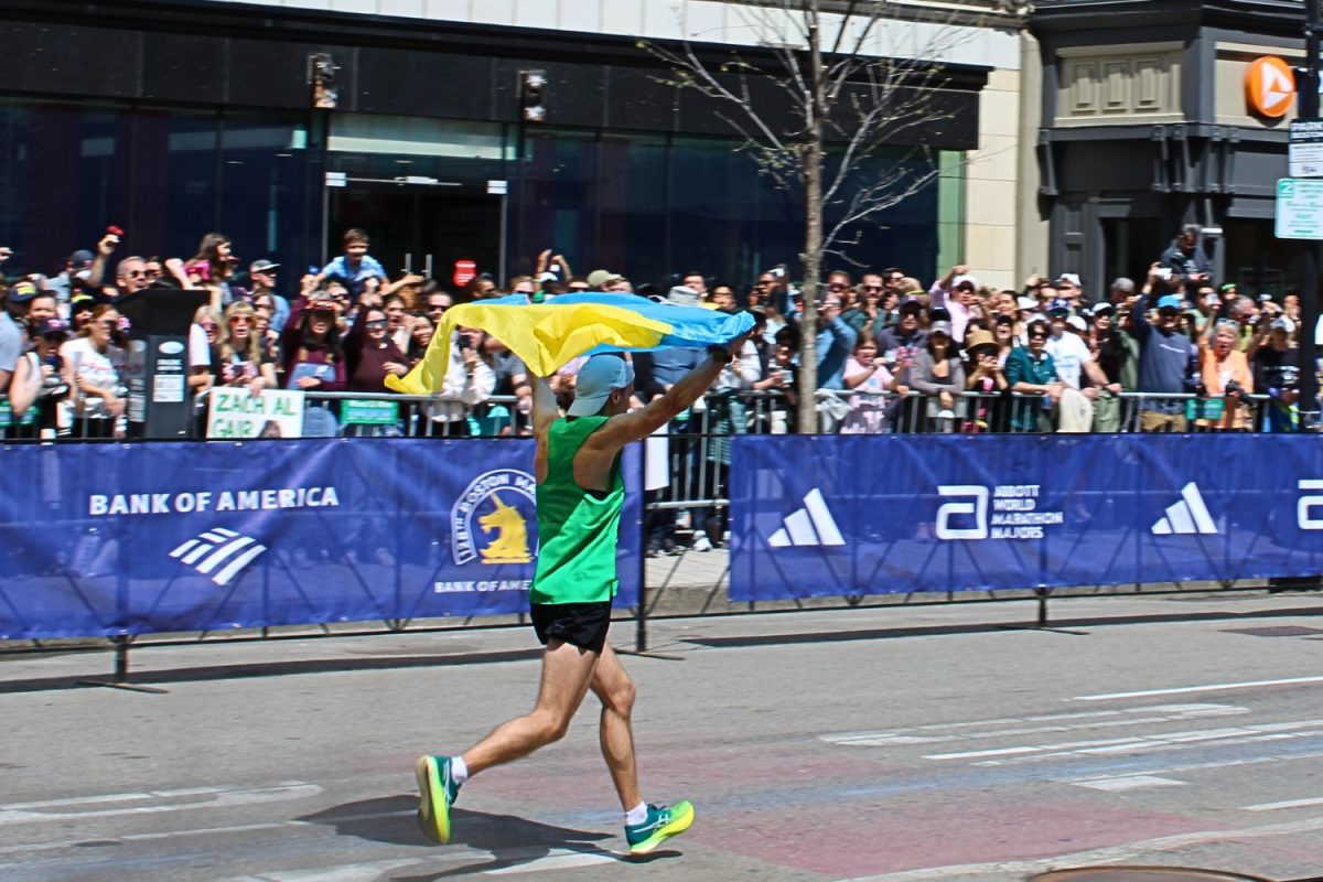 A runner holding a Ukrainian flag over his head moments before crossing the finish line of the 128th Boston Marathon held on Monday, April 15, 2024. (DJ Mara/Beacon Staff)