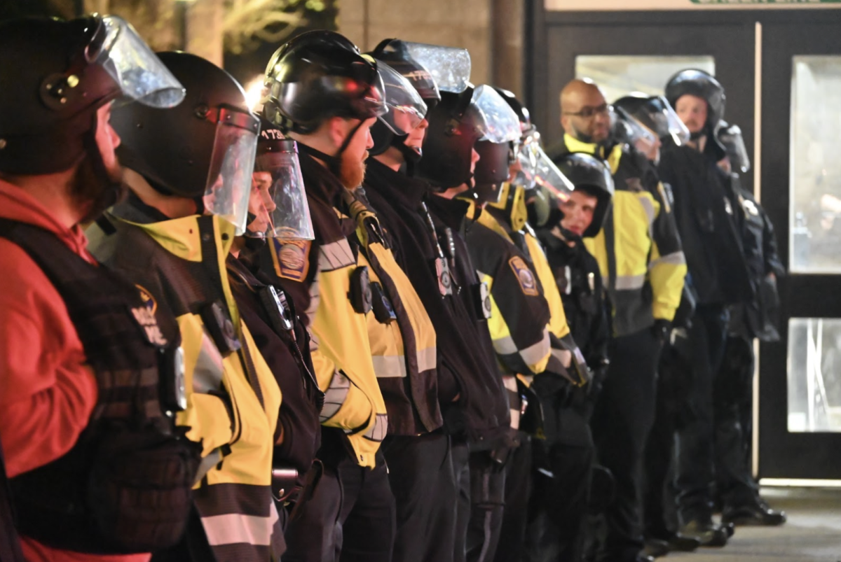 Police can be seen wearing face shields from a blockade on Boylston Street as they look onto a group of protesters near Tatte, where protesters have gathered after the 2B alley arrests on Thursday, April 25, 2024. (Nick Peace for the Beacon)