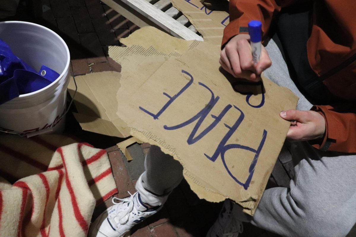 A protester writes “Peace” with a heart on a cardboard sign and holds it up as police prepare to enter the Boylston Place alley on Thursday, April 25, 2024. (Bryan Hecht/Beacon Staff)