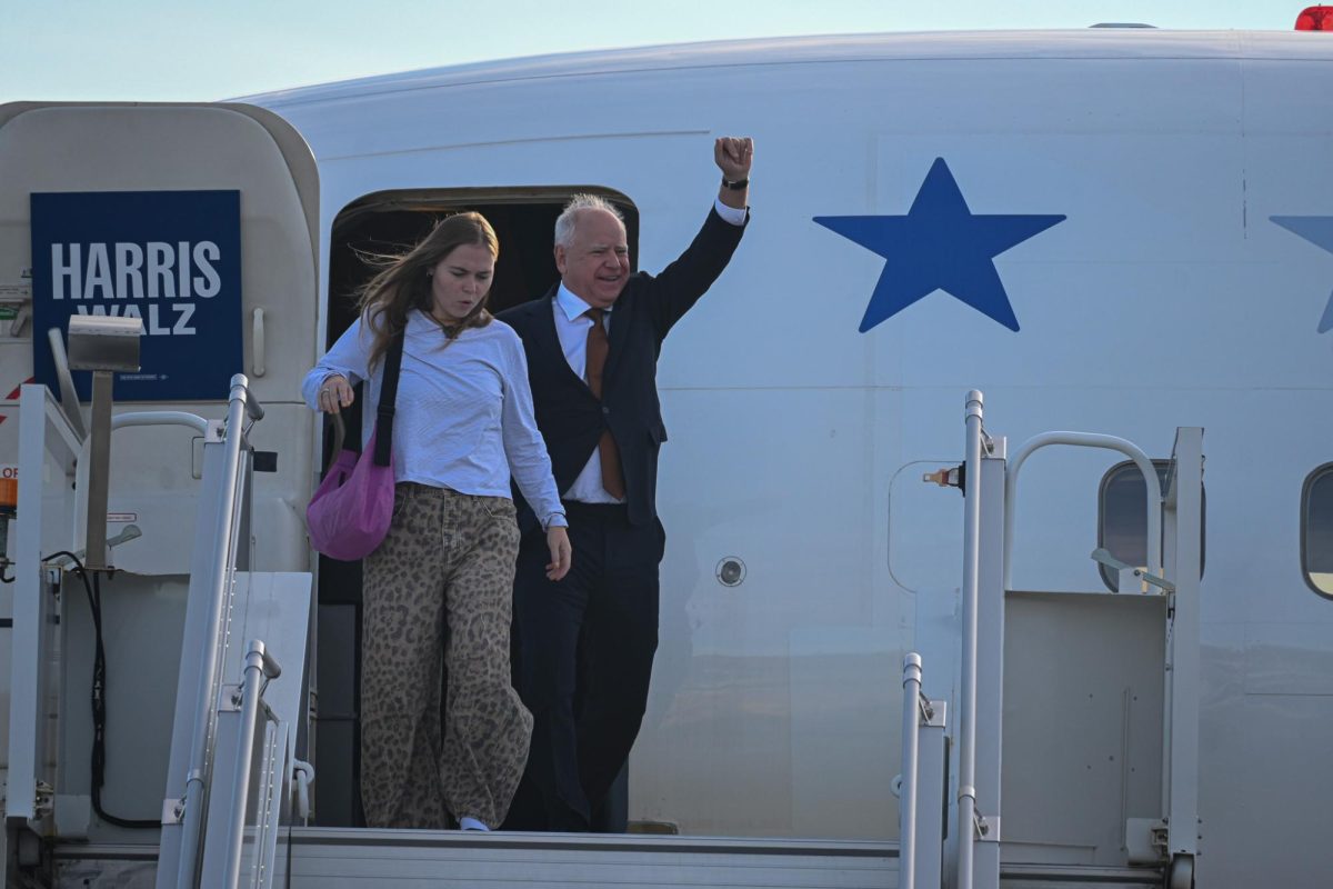 Tim Walz with a fist raised steps out of his airplane at Boston Logan International Airport on Oct. 20, 2024 (Nick Peace/ For the Beacon).