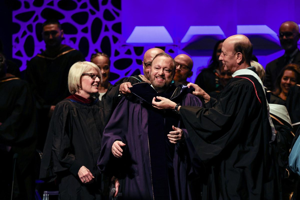 Emerson Trustees Ellen Calmas, left, Doug Holloway, behind, and Robert Miller, right, place an academic hood on Bernhardt at the investiture ceremony on Friday, March 22, 2024. (Ashlyn Wang/Beacon Staff)