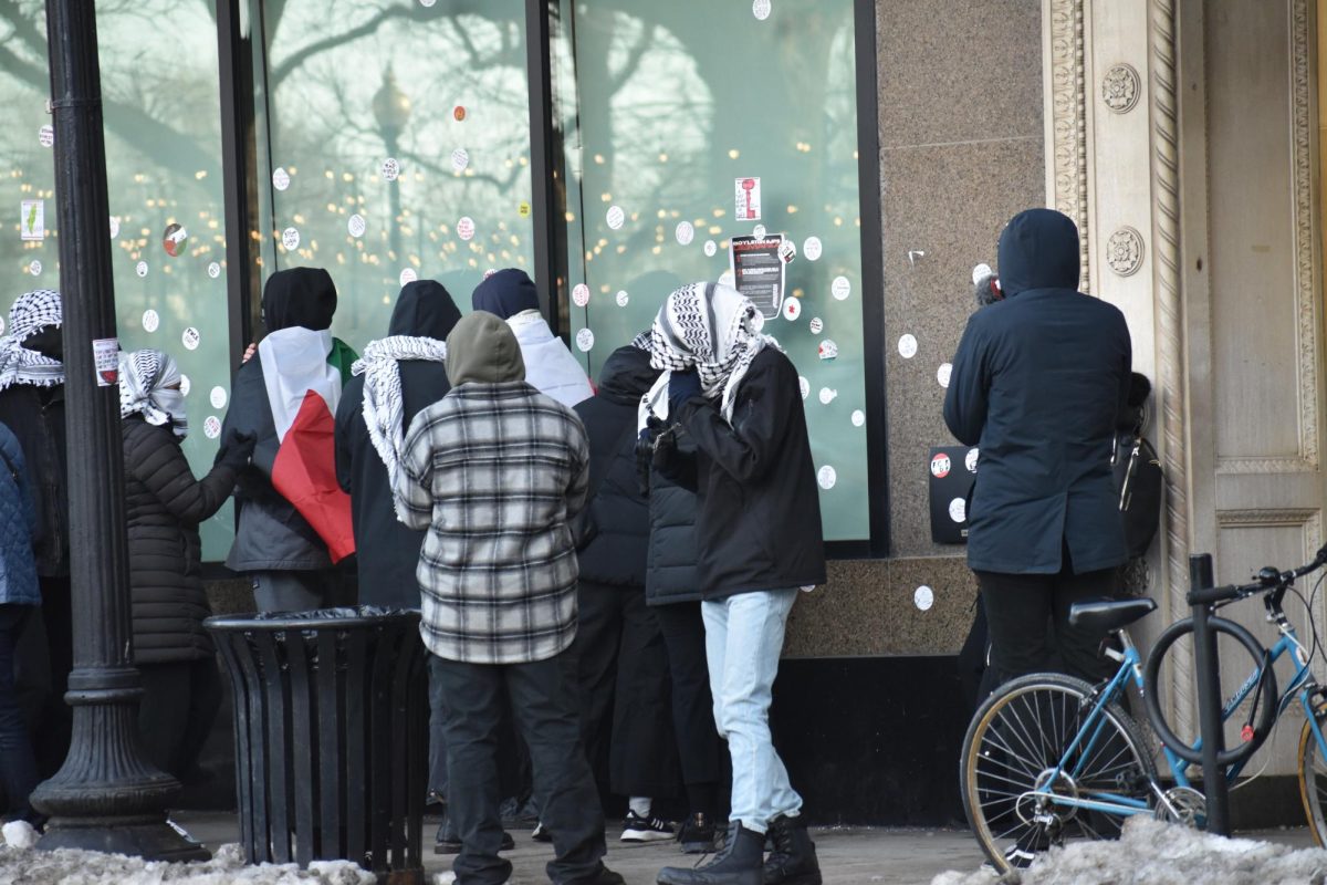 Protesters gather outside of Ansin building, glueing flyers listing their demands and hand-drawn stickers on the side of the building. (Madalyn Jimiera/ Beacon Staff)