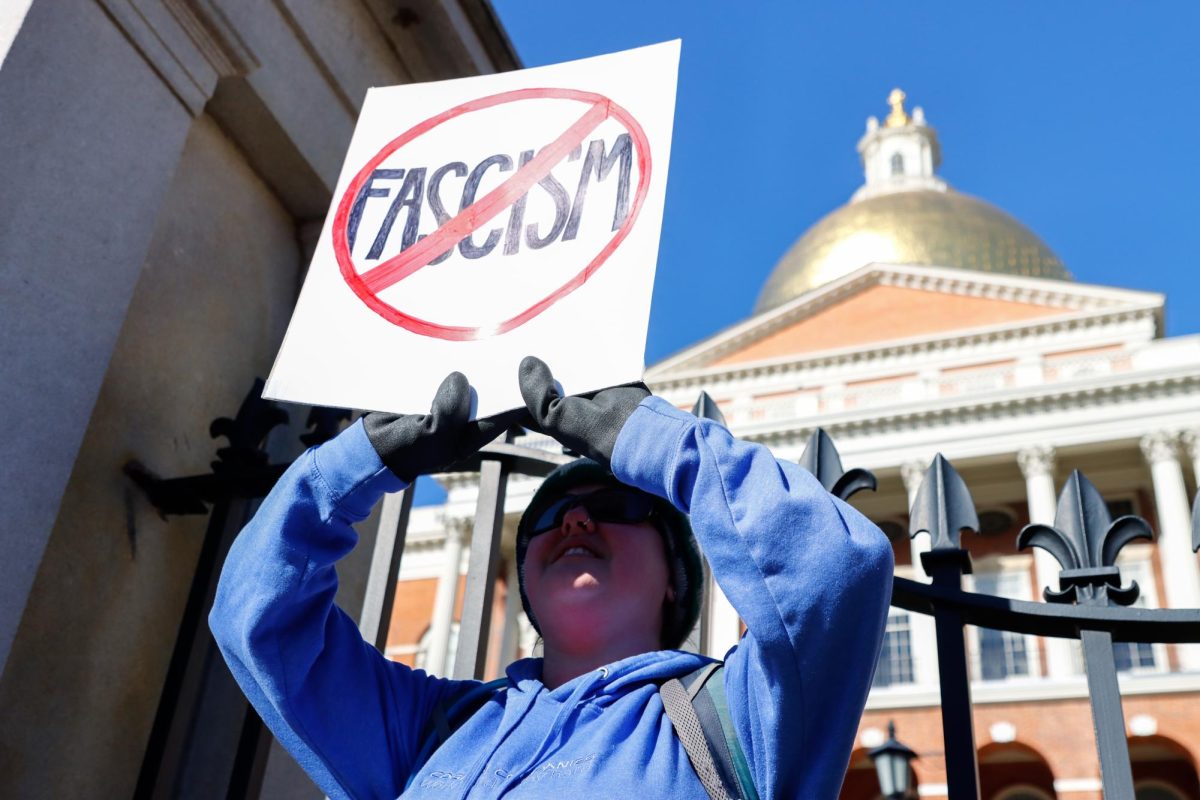 A protestor holds up a sign with the word “fascism” crossed out in front of the Massachusetts State House on Wednesday, Feb. 5, 2025. (Arthur Mansavage/ Beacon Staff)