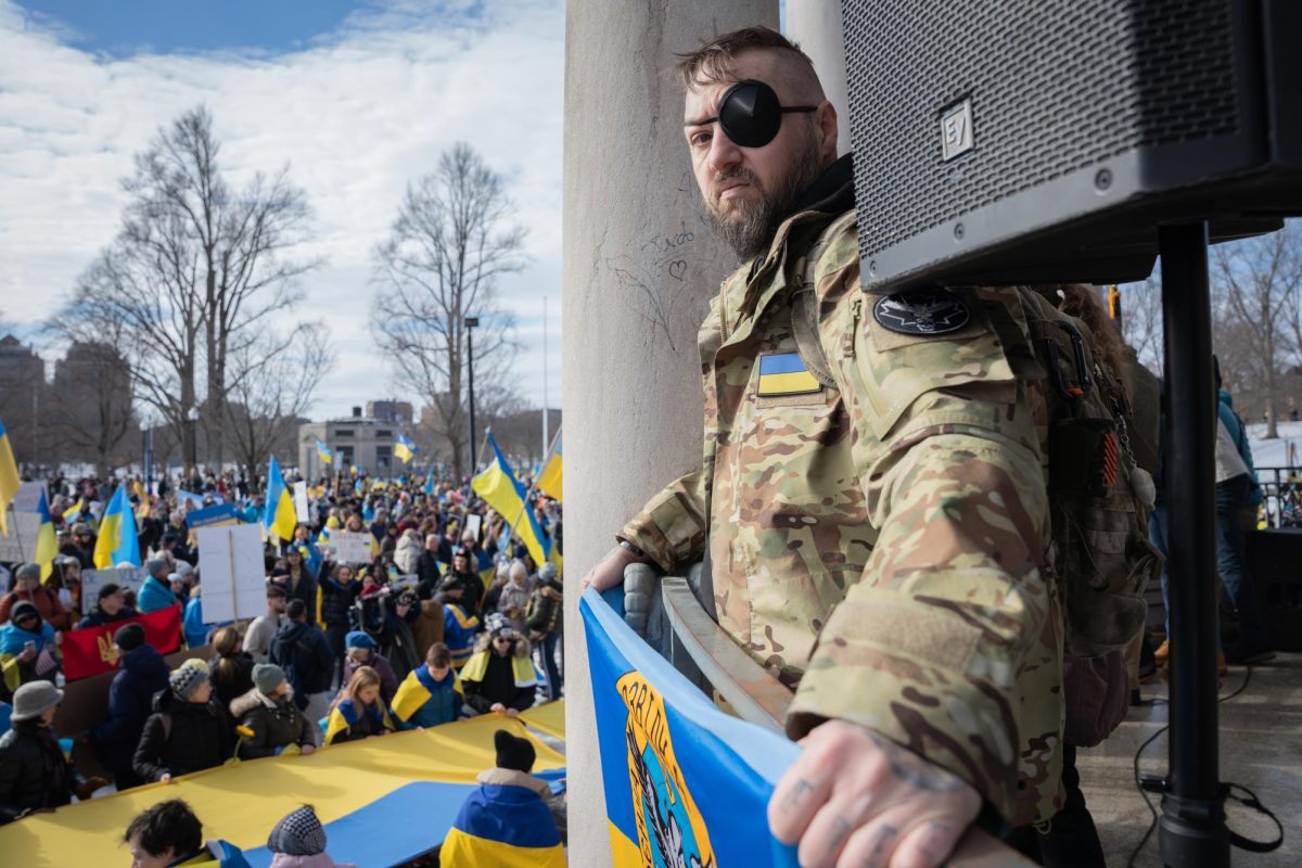 A Ukraine war veteran holds a "Defense Intelligence of Ukraine" flag at the Parkman Bandstand on Feb. 23 (Yogev Toby/ Beacon Staff)