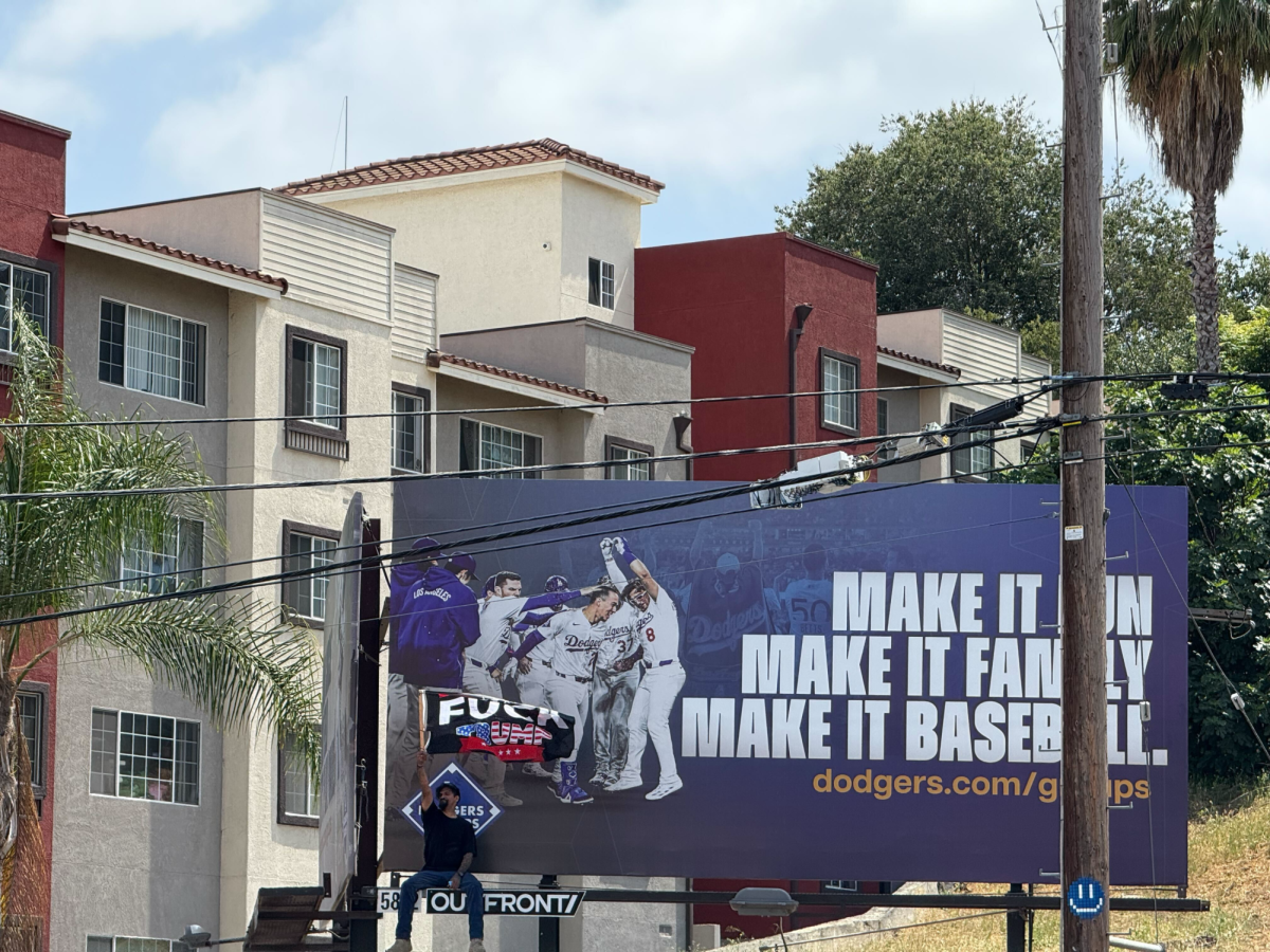 One protestor made his way to the edge of a Dodgers billboard, waving an anti-Trump flag while demonstrators rallied below (Jordan Pagkalinawan/ Beacon Staff).