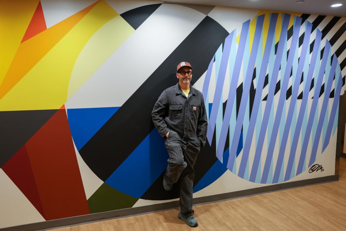 Artist Cyrille Conan stands in front of his mural titled “Mohrent,” located one flight down from the Piano Row lobby on the interior wall of the Fitness Center (Jacob Goldberg / Beacon Staff).
