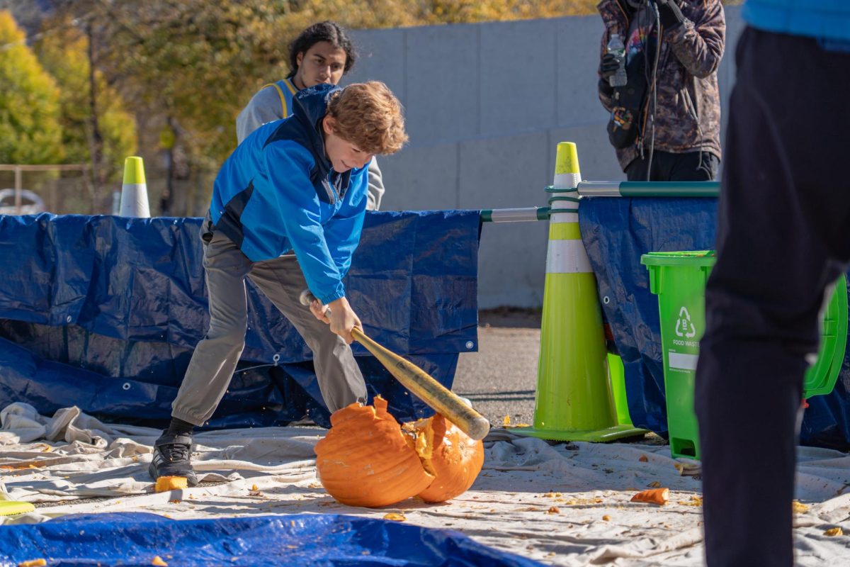 A child cracks a pumpkin down the center with a baseball bat. (Jay Guarino/ For The Beacon)