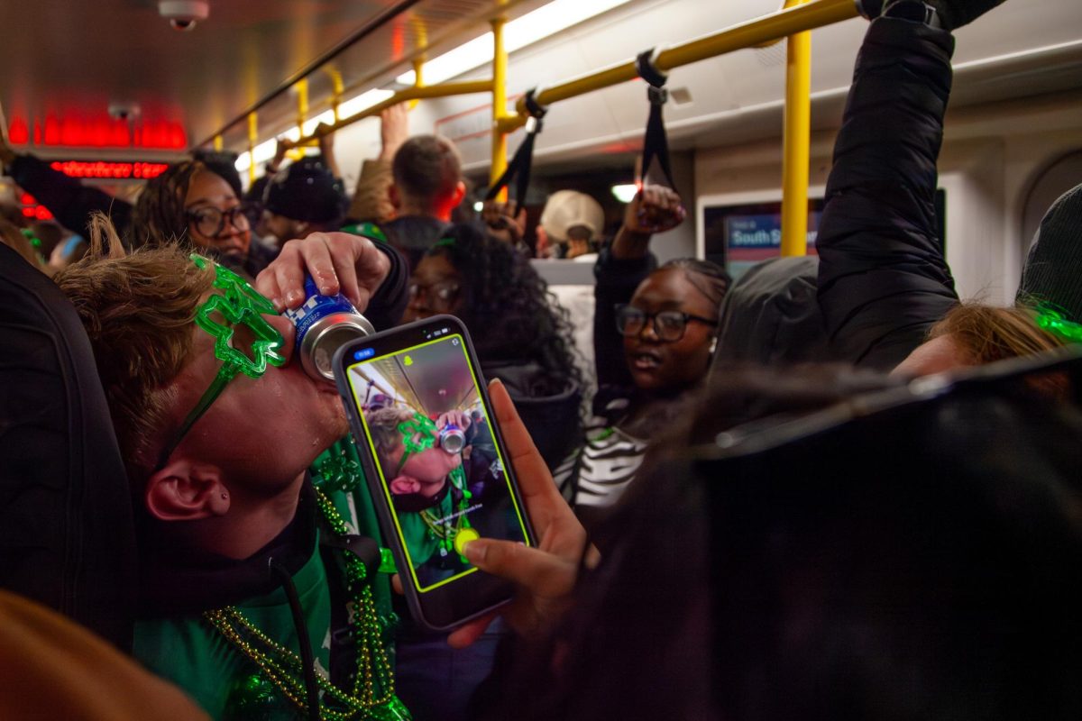 A parade goer shotgunning a beer on a crowded Red Line train (Iselin Bratz/ Beacon Staff)